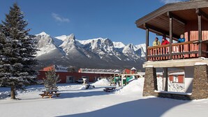 Área externa coberta de neve, com deck de madeira, mesa de piquenique e um prédio com fachada vermelha.