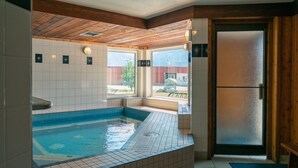 A spa area with a hot tub, tiled walls, wooden ceiling beams, and a view of the outside. - Cozy + Bright Canmore Room | Great Value! (Canmore)