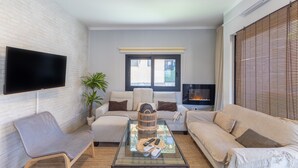 A living room with a flat-screen TV, two sofas, a glass coffee table, and a potted plant.