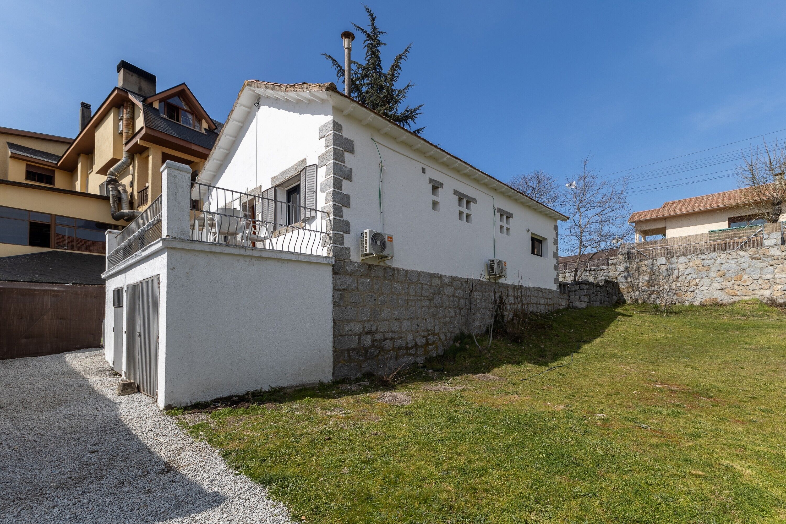 Un bâtiment blanc avec un socle en pierre, un petit balcon et une allée gravillonnée.