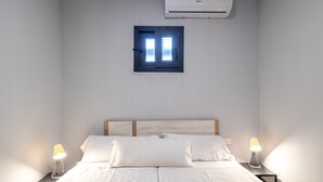 A bedroom with a bed, two bedside lamps, a window with a view, and an air conditioning unit.
