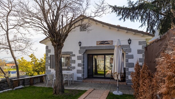 A house with a stone facade, a patio with chairs, and a tree in the yard.