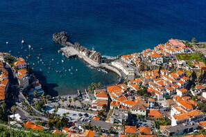 An aerial view of a coastal town with a prominent lighthouse, a curved harbor, and densely packed buildings with orange roofs. - Apartment in Câmara de Lobos | Privileged location (Câmara de Lobos)
