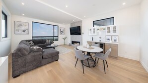 Un salon moderne avec un canapé gris, une table à manger avec des chaises, un téléviseur à écran plat fixé au mur et une cheminée.
