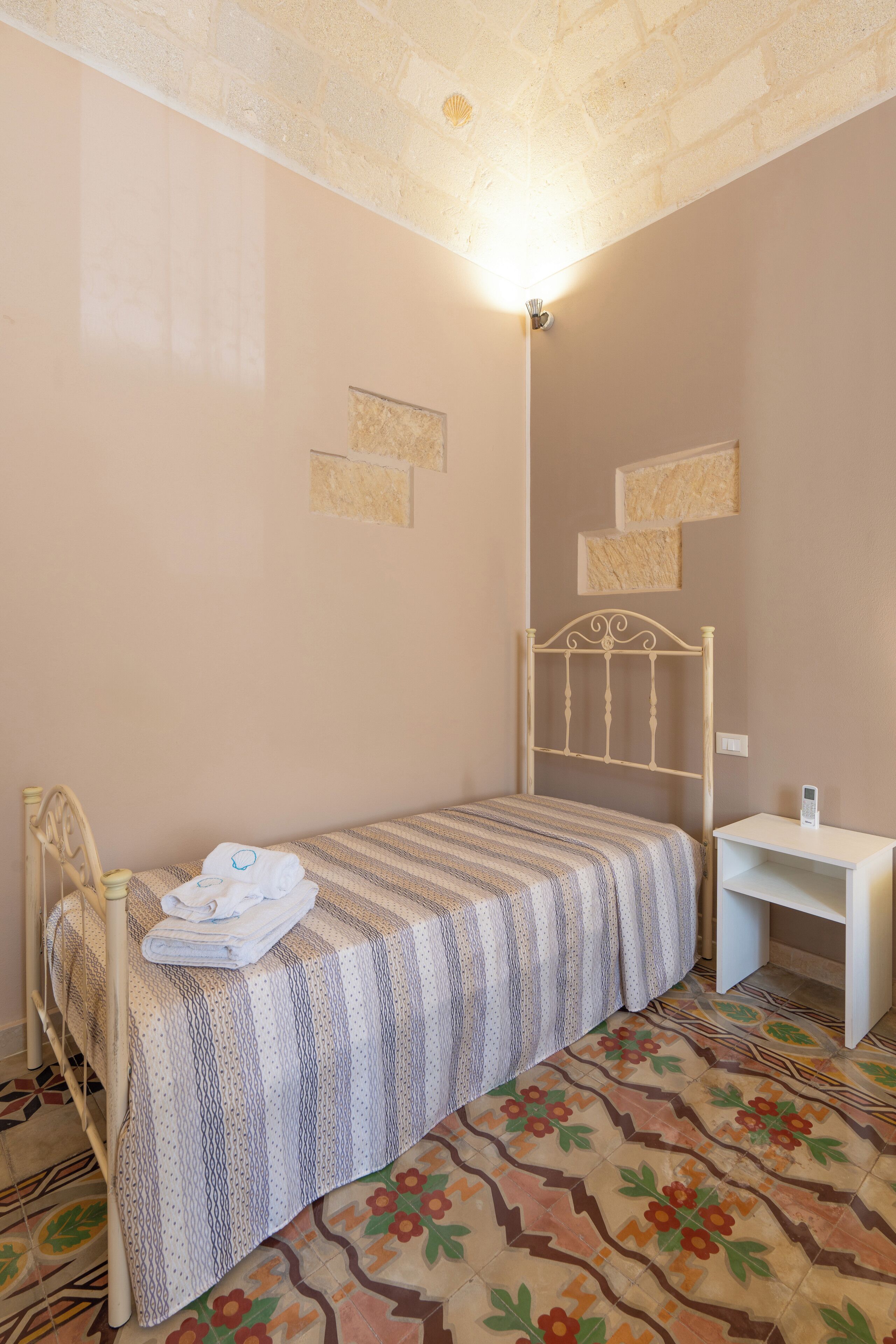 Ein kleines, ordentlich eingerichtetes Schlafzimmer mit einem Einzelbett, einem Nachttisch und einer Wandleuchte.