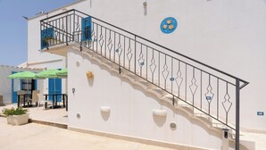 A white building with a staircase, outdoor seating, and a blue door. - Cozy, with garden, parking space, and 5 minutes from cornino bay beach (Sicilia)