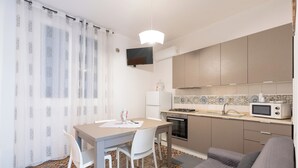 A compact kitchen with a dining area, a gray sofa, and patterned flooring. - Cozy, with garden, parking space, and 5 minutes from cornino bay beach (Sicilia)
