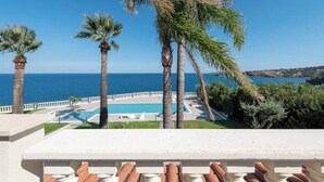Une vue sur la piscine, avec un ciel bleu dégagé, des palmiers et une vue sur la mer.