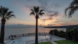 Un espace piscine avec des chaises longues et une vue sur la mer au coucher du soleil.
