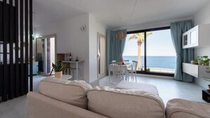 Un salon moderne avec un canapé, une table à manger et une vue sur la mer grâce à de grandes fenêtres.