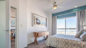 Un dormitorio con cama, escritorio, ventilador de techo y una ventana grande con vistas.