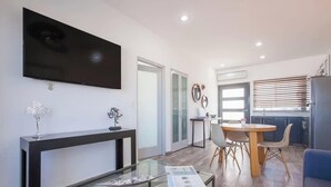 Una sala moderna con un televisor de pantalla plana, una mesa de centro de vidrio y un comedor con una mesa redonda y sillas.