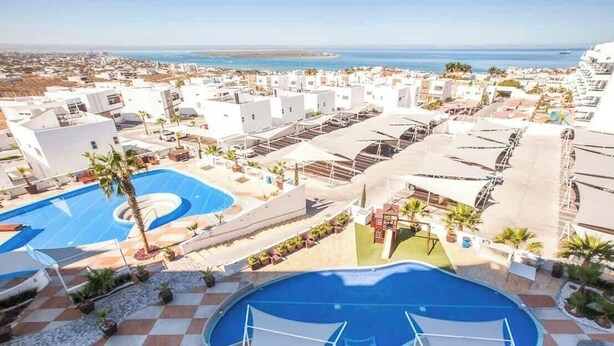 Un resort con varias piscinas, un patio a cuadros y vista al mar.