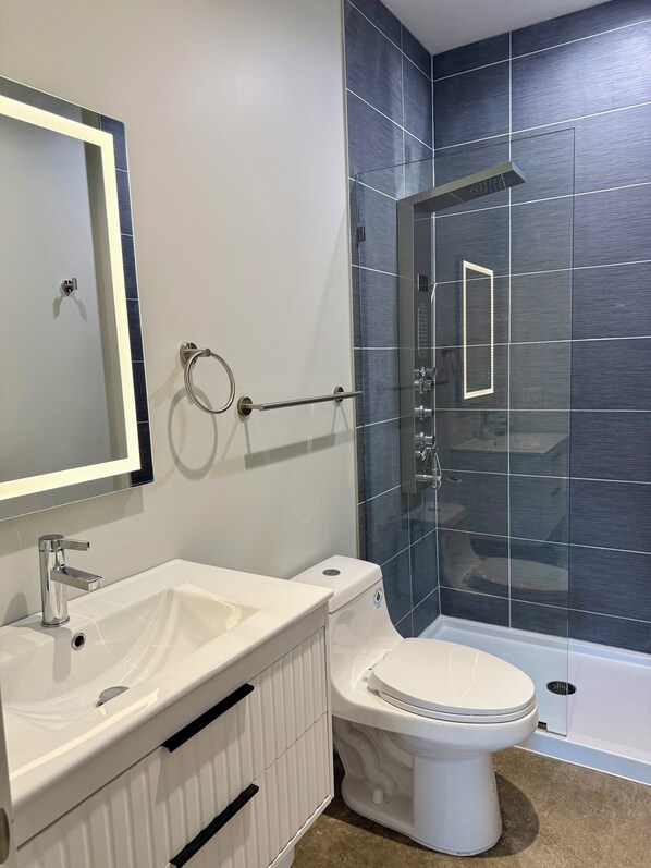 A bathroom with a white sink, a toilet, a glass shower enclosure, and a mirror.