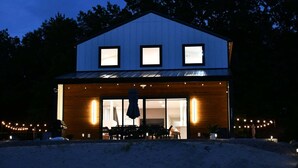 A modern two-story building with large windows, a covered patio area with outdoor seating, and a visible entrance.