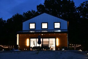Ein modernes, zweistöckiges Gebäude mit großen Fenstern, einer überdachten Terrasse mit Sitzgelegenheiten und einem gut sichtbaren Eingang.