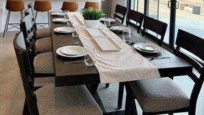 A modern dining room with a long table set for six, a ceiling fan, pendant lights, and a view of the outside.