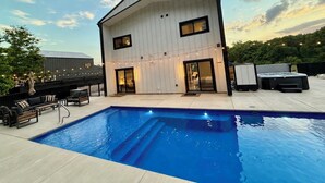 A modern two-story building with a swimming pool, outdoor seating, and string lights.