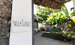 Een bord met de naam 'Wasanii' op een witte muur, dat een locatie of gelegenheid aangeeft.