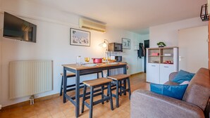 Een knus zithoekje met een eettafel, twee houten krukjes, een bank, een kast en een televisie.