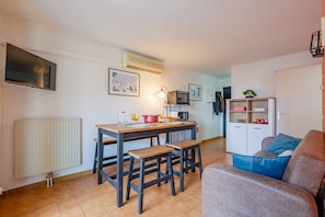 A small, cozy living area with a dining table, two wooden stools, a sofa, a cabinet, and a television. - FREJUS Apartment 5 minutes from town center and 10 minutes from the sea, (Fréjus)