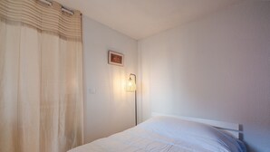 Een slaapkamer met een bed, een wandlamp en een gordijn.