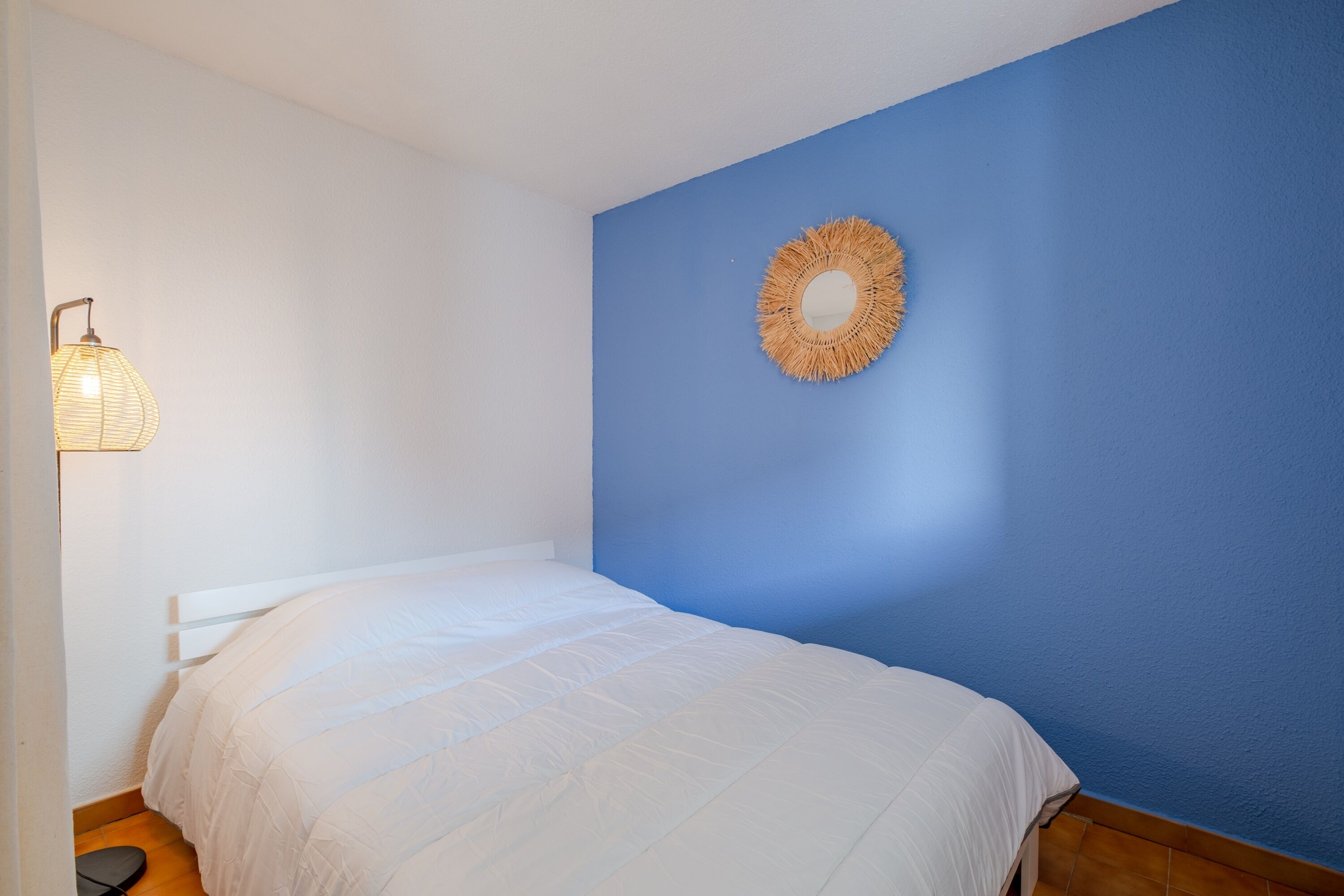 Une chambre à coucher avec un lit, une lampe fixée au mur et un élément décoratif suspendu au mur.