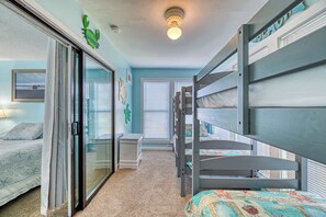 A bedroom with bunk beds, a sliding glass door, a small bedside table, and a bed with a patterned bedspread. - A Beach Escape- 1973 New River Inlet Rd (North Topsail Beach)