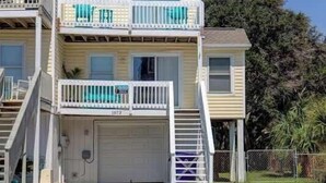 A two-story building with a garage, a balcony on the second floor, and a clear sky. - A Beach Escape- 1973 New River Inlet Rd (North Topsail Beach)