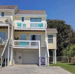 A two-story building with a garage, a balcony on the second floor, and a clear sky. - A Beach Escape- 1973 New River Inlet Rd (North Topsail Beach)