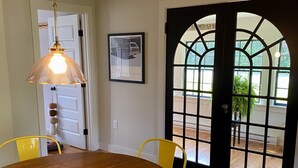 A dining area with a wooden table, yellow chairs, a hanging pendant light, and a large arched window. - Little Queen - 3 Bedroom Renovated Cottage in Chatham (Chatham)