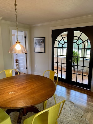 A dining area with a wooden table, yellow chairs, a hanging pendant light, and a large arched window. - Little Queen - 3 Bedroom Renovated Cottage in Chatham (Chatham)
