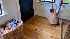 A room with a black door, a wicker basket with colorful towels, a wooden table, and a window with a view of greenery. - Little Queen - 3 Bedroom Renovated Cottage in Chatham (Chatham)