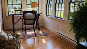 A room with a wooden floor, a chair, a table, a lamp, a basket, and a plant. - Little Queen - 3 Bedroom Renovated Cottage in Chatham (Chatham)