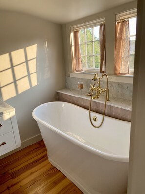 Ein Badezimmer mit freistehender Badewanne, einem Fenster mit Vorhängen und einer Marmorarbeitsplatte.