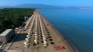 A beach with rows of umbrellas and sun loungers, a lifeguard tower, and a red lifeguard chair. - Mobilhome im Ferienpark mit Grosser Poolanlage (Orbetello)