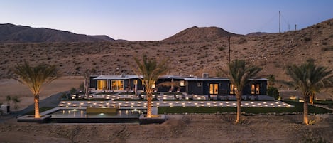 Une maison moderne avec une piscine, des palmiers et un paysage désertique.