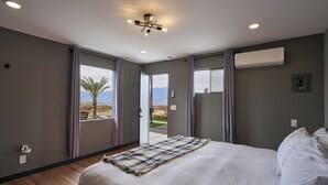 Une chambre dotée d’un grand lit, d’un luminaire au plafond, d’un appareil de climatisation et offrant une vue sur les palmiers et les montagnes par la fenêtre.