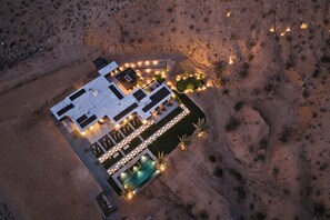 Vista aèria d'una casa moderna amb piscina, envoltada per un paisatge desèrtic.