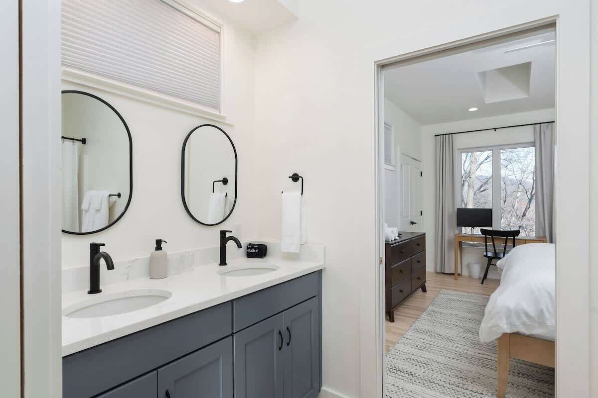 A modern bathroom with a double sink, two large mirrors, and a vanity with dark gray cabinets.