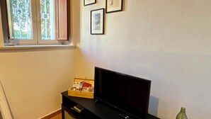 Un salon avec un téléviseur à écran plat posé sur un meuble noir, une fenêtre avec des rideaux et trois tableaux encadrés accrochés au mur.
