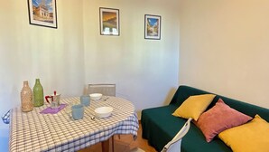 Une pièce chaleureuse avec une table à carreaux, un canapé vert et trois tableaux encadrés accrochés au mur.