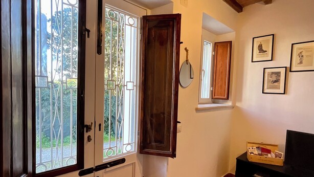 Une pièce avec une porte en bois, une fenêtre avec des barreaux en métal, un miroir, un meuble en bois et un meuble TV noir.