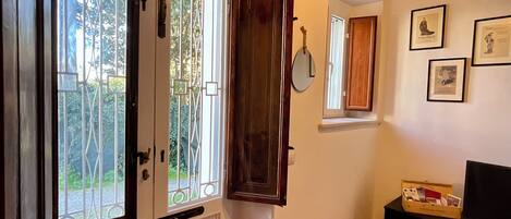 A room with a wooden door, a window with metal bars, a mirror, a wooden cabinet, and a black TV stand.