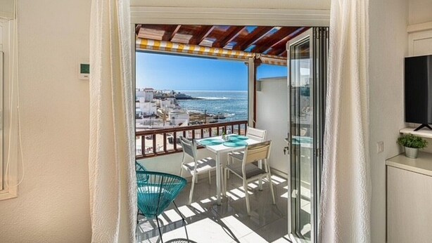 A balcony with a table and chairs, a TV, and a view of the sea and buildings. - Ocean View La Caleta (La Caleta)