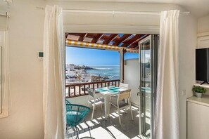 Un balcon avec une table et des chaises, un téléviseur et une vue sur la mer et les bâtiments.