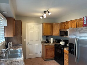 A kitchen with wooden cabinets, a stainless steel refrigerator, a microwave, a stove, and a sink. - Serene 3-bedroom house with AC in charming Aurora (Aurora)