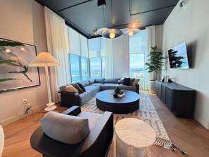 A modern living room with a sectional sofa, a round coffee table, and a large window offering a city view. - Live the Miami Experience | Prime Location Suite (Miami)