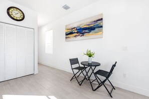 Une pièce avec un placard blanc, une horloge, un tableau et une table avec des chaises.