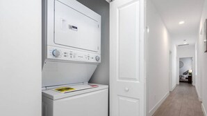 Une buanderie équipée d’un lave-linge et d’un sèche-linge à chargement frontal, d’une porte et d’un couloir menant à une autre pièce.